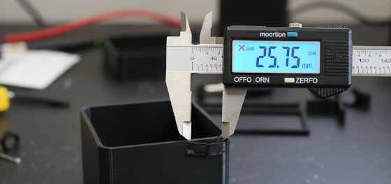 Digital caliper measuring a squished bottom layer of a plastic printed box revealing deviations